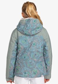La chaqueta de estampado floral presenta un diseño en azul y verde pastel con capucha gris. Fabricada con un tejido texturizado, tiene un corte holgado.