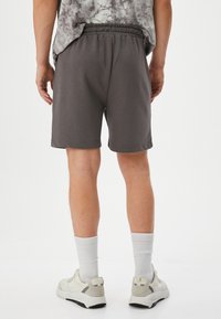 Graue Baumwollshorts mit einem elastischen Bund, die einen lockeren Sitz und eine mittellange Länge bis zum Oberschenkel haben, kombiniert mit weißen Socken und Turnschuhen.