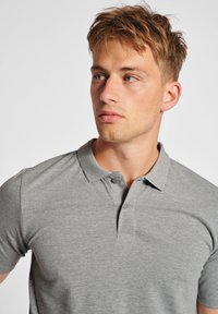 Polo grigio con collo a camicia, caratterizzato da due bottoni, realizzato in un tessuto liscio con una sottile texture melange.