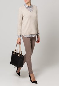Pull beige avec un col en V sur une chemise à motifs, associé à un legging taupe et des chaussures noires à talons hauts. Sac à main noir avec des bretelles.