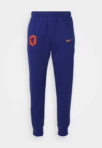 Námořnické modré tepláky s elastickým pasem, s oranžovým logem Nike a holandským lvem na levém stehně. Dokončeno ribbanými manžetami.