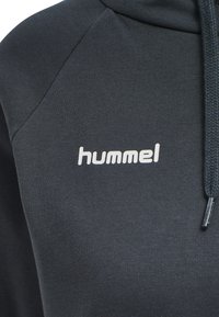 Czarna bluza z ribbed teksturą, z wyraźnym białym logo "hummel". Kaptur ze sznurkiem i kontrastowe przeszycia widoczne.