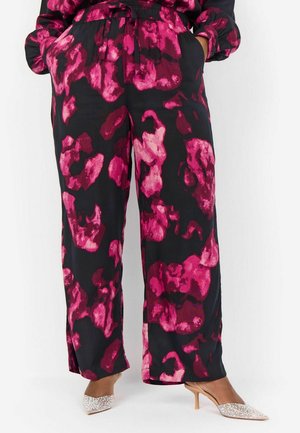 Pantalons noirs avec un grand motif abstrait rose ; design à jambes larges ; taille élastique avec cordon de serrage ; associés à des mules à talons pailletés.