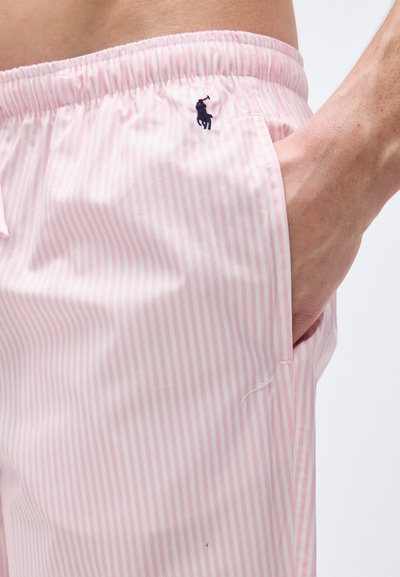 Άνδρας που φορά ροζ και λευκό κάθετα ριγέ σορτς με ελαστική μέση και μπλε κεντημένο λογότυπο παίκτη πόλο, με το χέρι στην τσέπη.