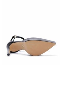 Zapato de tacón alto de charol negro con punta afilada, correa en el tobillo y una suela beige lisa, que presenta una silueta elegante y un mínimo de detalles.