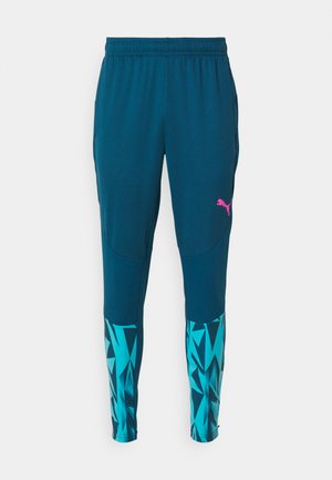 Mannelijke sportbroeken in donker teal stof met een tekstuurafwerking. Voorzien van een roze logo en geometrische blauwe accenten op de benen. Elastische tailleband.