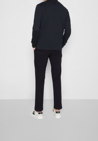 Svart långärmad skjorta och svarta byxor med fickor, ihop med vita sneakers med svarta detaljer. Slät tyg, figurnära design.