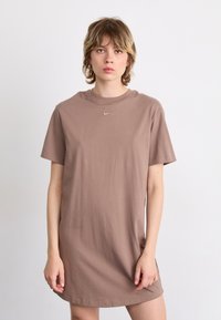 Barna pamut t-shirt ruha laza szabással, kerek nyakkivágással, rövid ujjakkal és egy kis Nike logóval a mellkason. Sima textúra.