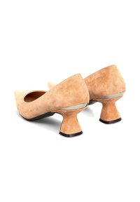 Tacones de ante beige con un diseño de punta afilada y un tacón acampanado único. Un acento plateado en la base añade detalle. Acabado texturizado en la superficie.