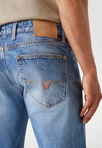 Lichtblauwe denim jeans met een leren label op de taille. Opvallende driehoekige rode en witte patch op de achterzak. Casual ontwerp.