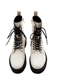 Botas de tacón blancas de piel con cordones negros, punta redonda y suela de goma negra con un patrón texturizado. Cierre de cremallera en el lateral.