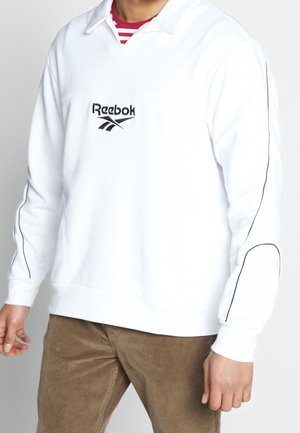 Biała bluza z pulowerem wykonana z bawełnianej mieszanki, z kołnierzem, czarnym logo Reebok na piersi oraz czarnym obszyciem wzdłuż rękawów.