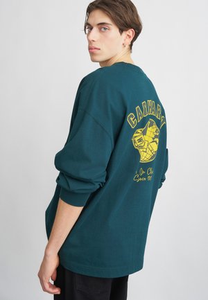 Dunkelgrüner langärmeliger Sweatshirt aus Baumwolle mit einem großen gelben Grafik auf der Rückseite, die den Text "CARHARTT" und ein Globus-Design zeigt.