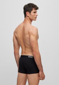 Black cotton boxer trunks with a fitted design and a branded waistband featuring "BOSS" in white. Smooth texture, no visible patterns.