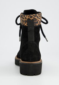 Botte chelsea noire en suède avec un revers en imprimé léopard texturé, un devant à lacets et une semelle en caoutchouc noire robuste pour une meilleure adhérence.