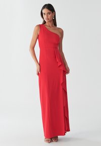 Vestido rojo de un solo hombro con corpiño entallado y un detalle de volantes en un costado. Confeccionado con tela suave, cuenta con un diseño hasta el suelo.