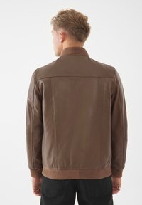 Giacca di pelle marrone con colletto e polsini a costine, caratterizzata da una superficie liscia e un design aderente, vista da dietro su uno sfondo bianco.