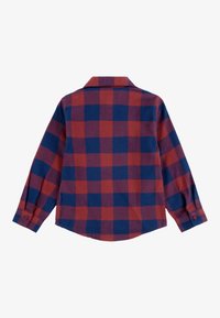 Camisa de franela de manga larga en un patrón de cuadros rojo y azul marino. Presenta un collar clásico y puños con botones. Textura suave y corte relajado.