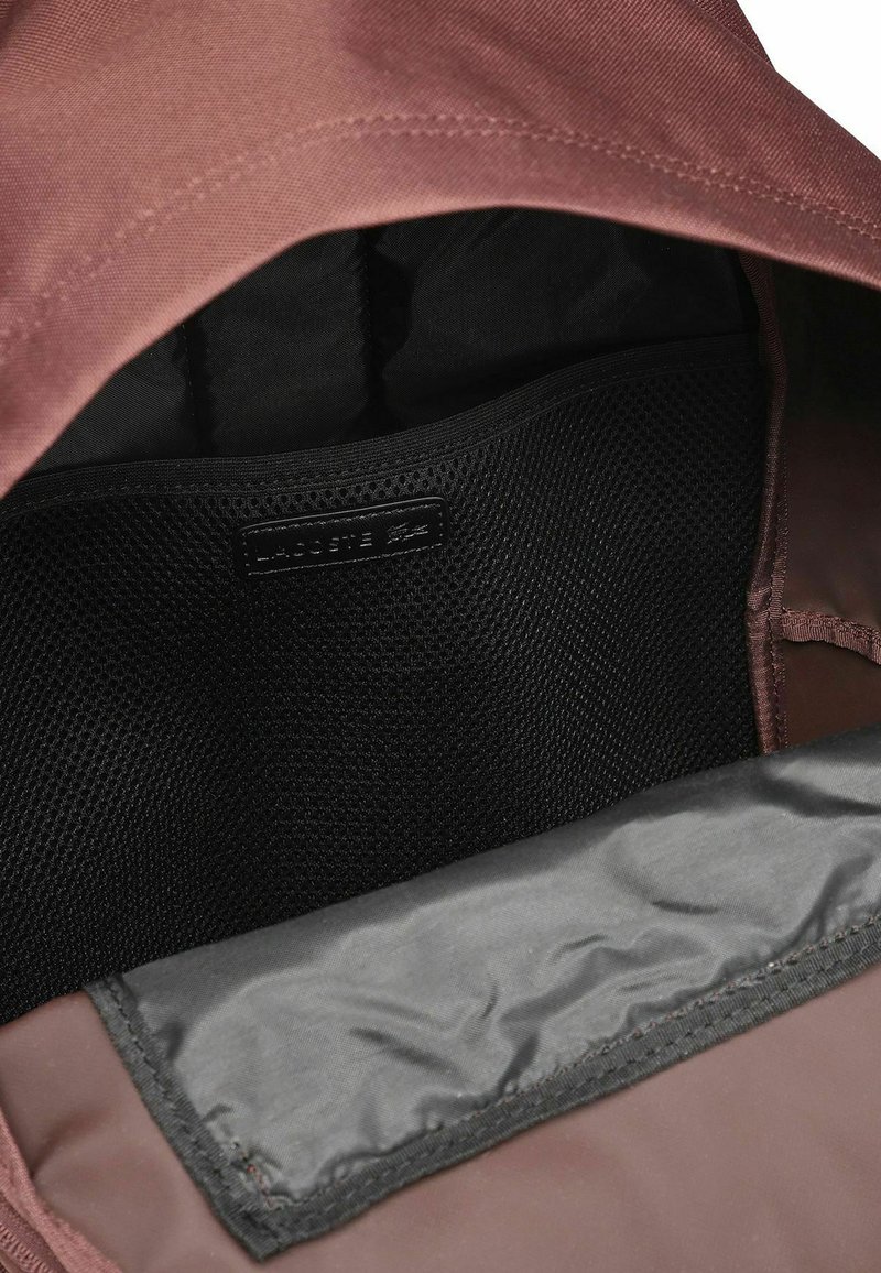 Brown backpack interior, featuring a black mesh pocket and smooth dark lining. The top has a fold with visible stitching details.