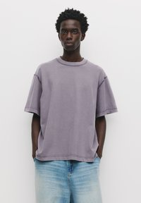 Løst siddende t-shirt med korte ærmer i dæmpet lavendelfarve, med rund halsudskæring og kontrasterende syninger.