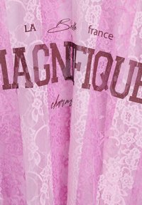 Rosa Spitzenstoff mit floralen Mustern, versehen mit kräftigem braunem Text "MAGNIFIQUE" und "LA Belle france", der sich über durchsichtige Lagen legt.