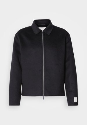 Black jacket with a collar, front zip closure, and a square cut. Made from soft fabric, featuring a small tag on the left sleeve.