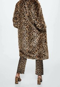 Cappotto in pelliccia sintetica con stampa leopardata e silhouette oversize, indossato sopra pantaloni abbinati con stampa leopardata, abbinato a sandali con tacco chunky.