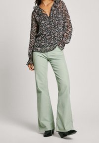 Bloemenprint blouse met gerimpelde halslijn, gecombineerd met mintgroene, uitlopende broek. Gestructureerde stof en contrasterende zwarte en gekleurde patronen.