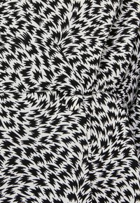 Tecido estampado em preto e branco com formas em zigue-zague, apresentando uma textura suave e um detalhe de botão, adequado para design de vestuário.