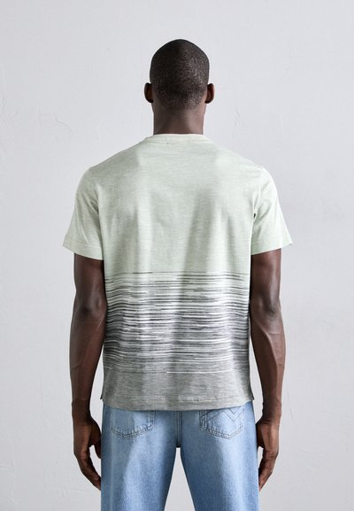 Lys grønn t-skjorte med korte ermer, med et gradientdesign som går over til grå horisontale striper nederst. Myk tekstur.