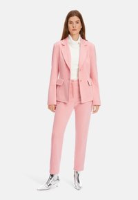 Rosa Cord-Blazer mit Revers, kombiniert mit passenden Hosen. Das Outfit wird durch glänzende silberne Ankle Boots ergänzt.