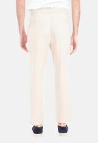 Pantaloni beige chiaro con taglio dritto, realizzati in morbido tessuto, con tasche posteriori e indossati con scarpe blu scuro.