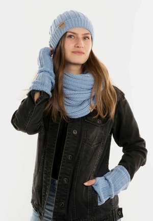 Lichtblauwe gebreide beanie, sjaal en vingerloze handschoenen gecombineerd met een zwarte spijkerjack. Geribbelde textuur, met een klein logo op de beanie.