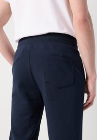 Pantaloni della tuta blu navy con una finitura testurizzata, dotati di una tasca posteriore e di una vita elastica per comfort e vestibilità.