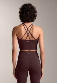 Burgundska športna modrček z križnimi naramnicami, gladka tekstura in logotip blagovne znamke. Ujemajoče se visokotakšne legice v isti barvi.