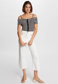 Top de rayas en blanco y negro sin mangas, con botones en la parte delantera, combinado con pantalones cortos de tiro alto en blanco y sandalias de tacón cuadrado doradas.