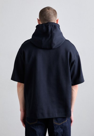 Námornícky mikina s kapucňou a krátkymi rukávmi, vyrobená z bavlneného zloženia. Má voľný strih a minimalistický dizajn.