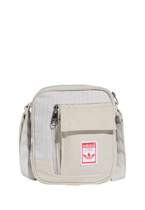 Borsa a tracolla in tela beige con righe verticali, tasca frontale con zip e patch del logo rosso Adidas. Tracolla regolabile per versatilità.