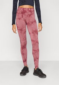 Legíny s bordovým tie-dye vzorom, hladkým povrchom a vysokým pásom, v kombinácii s čiernymi športovými topánkami a tmavomodrým dlhým rukávom.