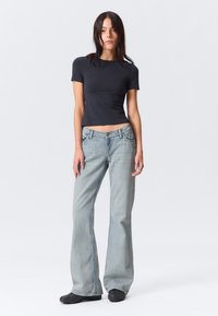 Schwarzes, tailliertes Kurzarmoberteil kombiniert mit hellblauen, ausgestellten Jeans. Die Jeans verfügen über ein traditionelles Fünf-Taschen-Design und sichtbare Nähte.
