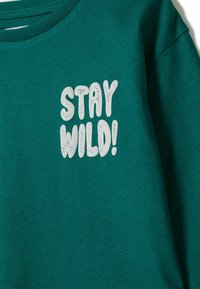 Tīrā zilās krāsas džemperis ar baltiem bold burtiem "PALIEC KURŠ" drukātiem augšējā krūtī novecojušā fonta stilā.