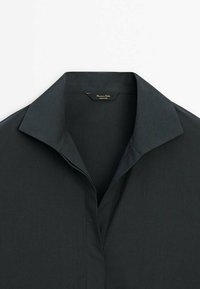 Chemise collerette gris foncé en tissu lisse et texturé. Présente un décolleté en V profond et une étiquette portant la mention "Massimo Dutti" à l'intérieur du col.