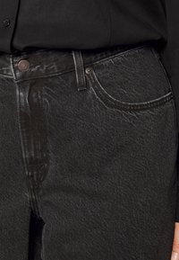 Schwarze Denim-Jeans mit einer feinen Textur, fünf Taschen, Metallknopfverschluss und Kontrastnähten in der Nähe der Taschen.