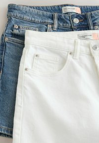 Deux paires de shorts taille mi-haute, l'une blanche et l'autre en denim bleu, superposées avec les tailles, poches, boutons et étiquettes visibles.