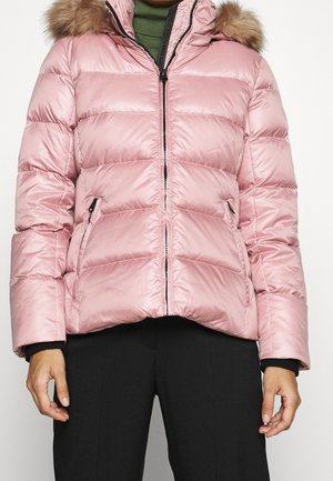 Hellrosa gesteppte Steppjacke mit Reißverschluss vorne, seitlichen Taschen und Kapuze mit Fellbesatz, getragen über grünem Oberteil und schwarzer Hose.