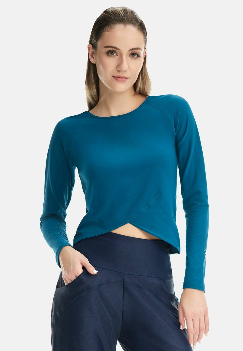 Teal long-sleeve shirt with a rounded neckline, featuring a crossover front design. Soft, stretchy fabric accentuates the figure.
