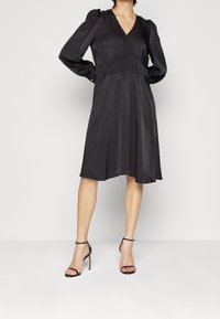 Svart klänning med långa puffärmar, V-ringning och figurnära bodice. Tillverkad av ett mjukt, följsamt tyg med en utsvängd kjol. Minimalistisk design.