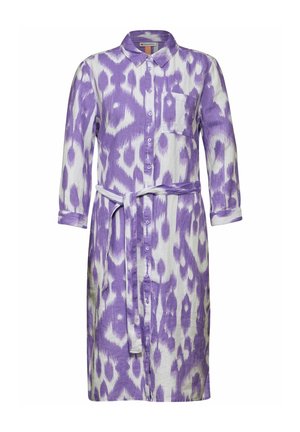 Pakai baju dress panjang dengan kancing berwarna ungu dan putih dalam pola ikat, dilengkapi dengan kerah dan pinggang yang diikat. Memiliki satu saku dada dan lengan yang dilipat.