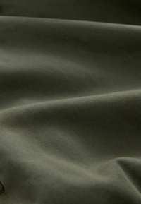 Tissu vert olive à texture lisse, présentant un léger éclat et un tombé doux, mettant en valeur des plis et des froissements délicats.