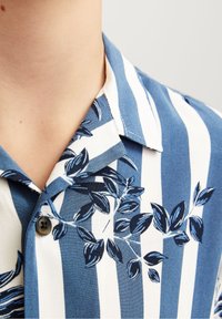 Niebiesko-biała w paski koszula z krótkim rękawem z kwiatowym wzorem liści, z kołnierzykiem i zapięciem na guziki. Gładka faktura materiału.